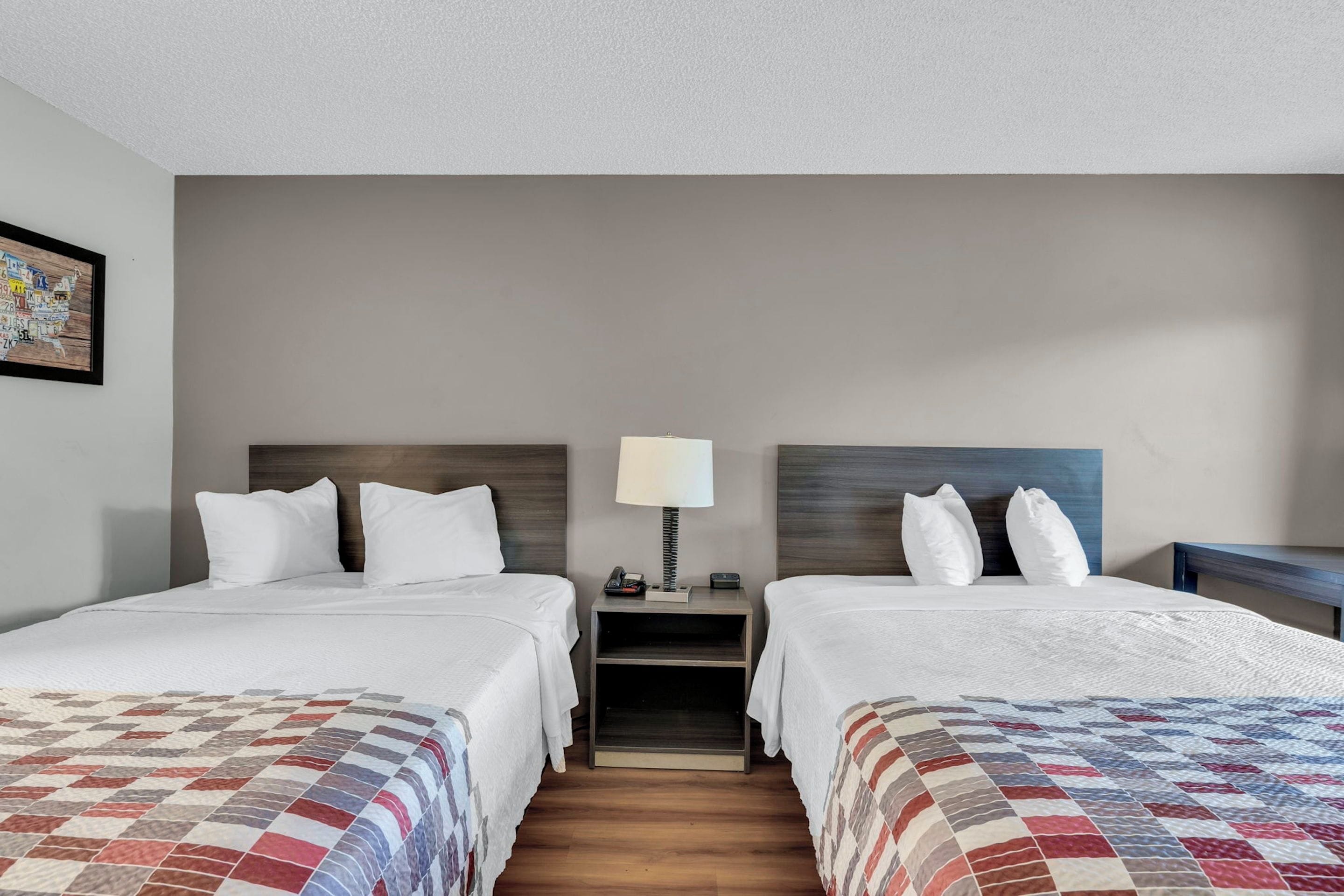 A hotel room with two beds, a nightstand with a lamp, and a wall-mounted picture.