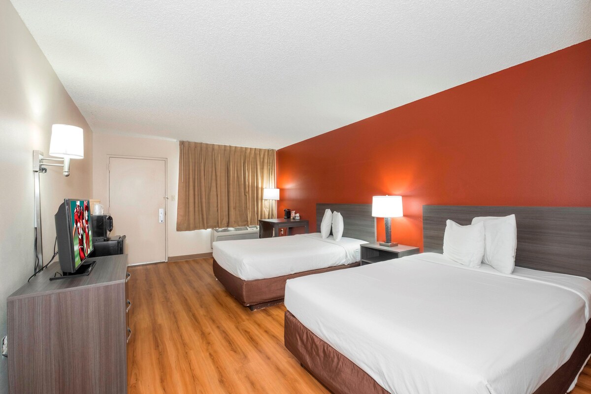 A hotel room with two beds, a desk with a television, and a bathroom.
