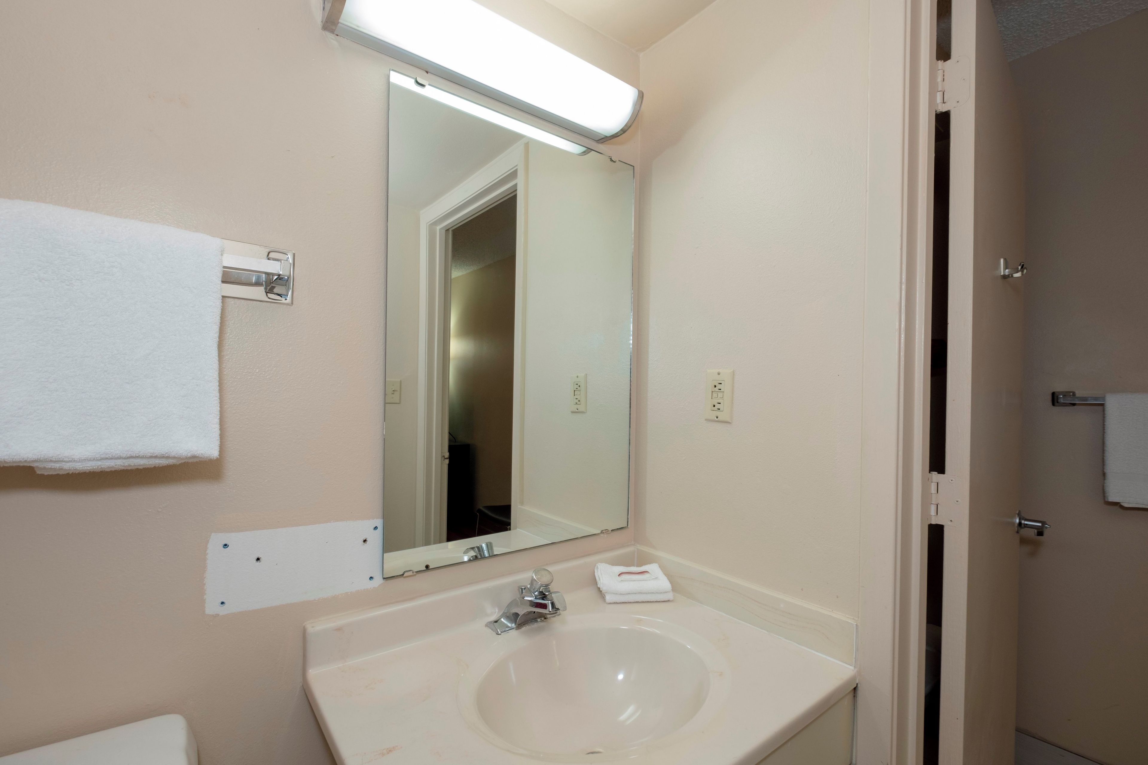 Un baño con lavamanos blanco, espejo y perchero.