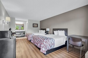 Habitación de hotel con una cama grande, un escritorio, una silla, una kitchenette y una ventana con vistas a zonas verdes.