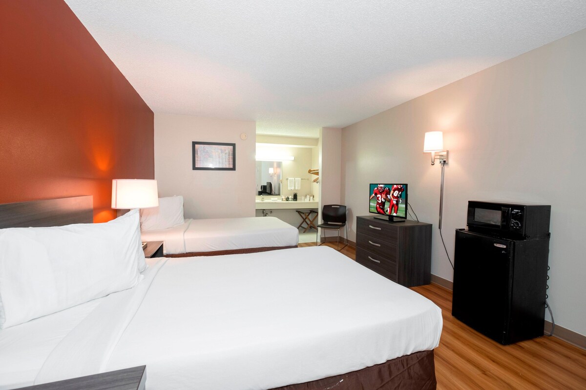 A hotel room with two beds, a desk, a chair, a television, and a microwave.