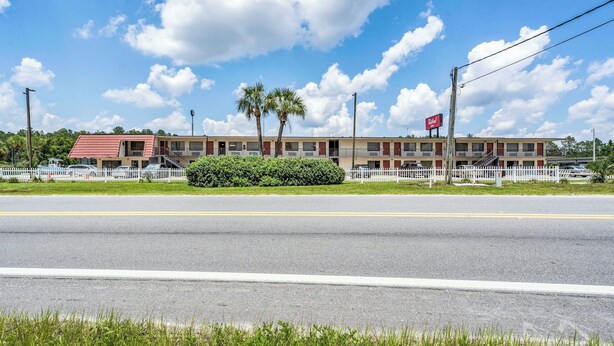 A motel with a red roof, white picket fence, and palm trees. - Red Roof Inn MacClenny (MacClenny)