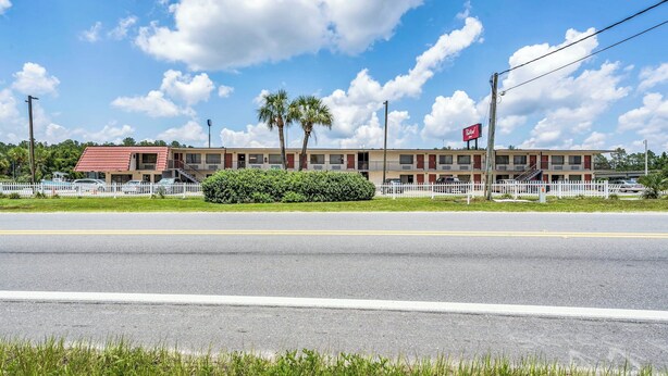 A motel with a red roof, white picket fence, and palm trees. - Red Roof Inn MacClenny (MacClenny)