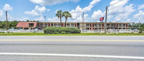 A motel with a red roof, palm trees, and a white fence.