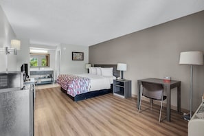 A hotel room with a bed, bedside tables, a desk, a chair, and a view of greenery outside. - Red Roof Inn MacClenny (MacClenny)