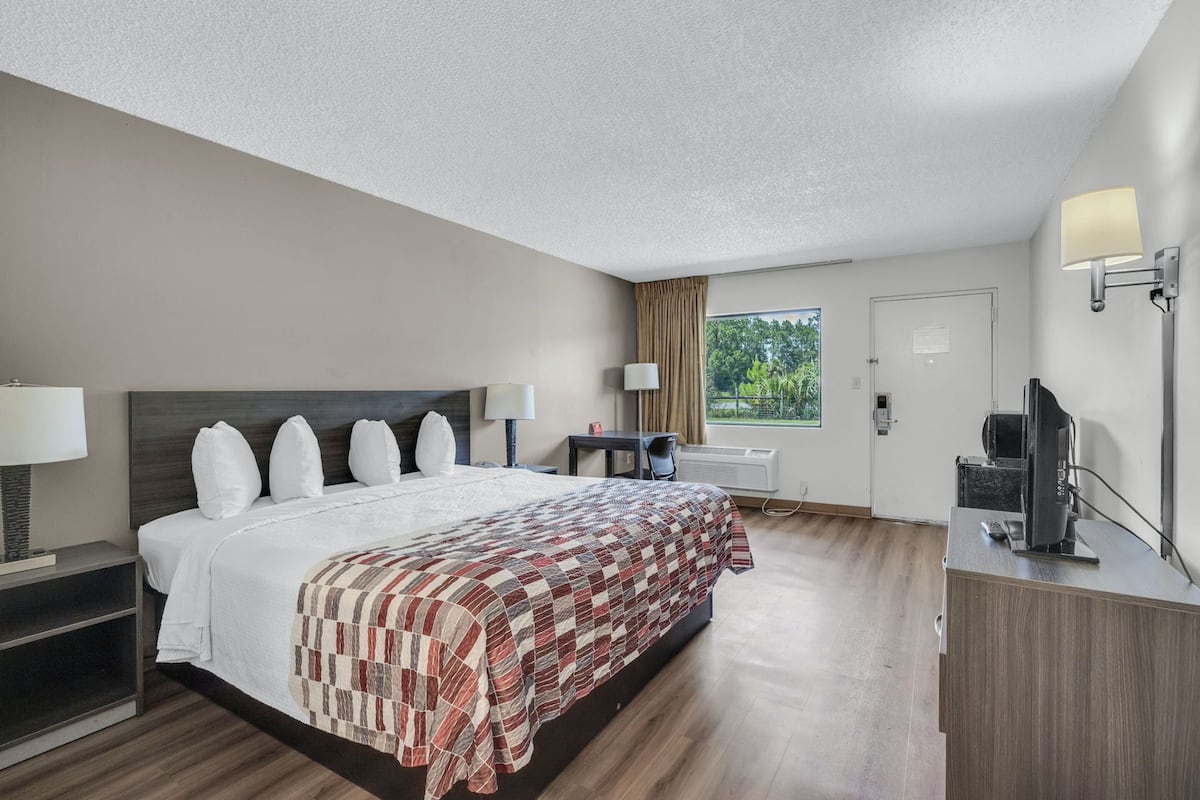 Hotellihuone, jossa on suuri sänky, yöpöydät, työpöytä tietokoneella sekä ikkuna, jossa on verhot.