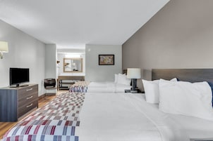 Habitación de hotel con cama, mesitas de noche, escritorio, silla, televisión y baño visible a través de una puerta abierta.