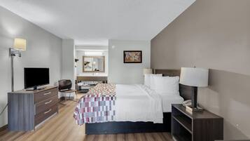 Habitación de hotel con cama, mesita de noche, lámpara, televisor, cómoda y espejo.