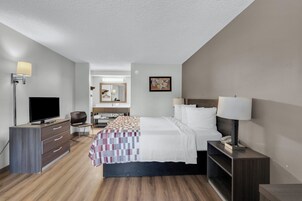 Habitación de hotel con cama, mesita de noche, lámpara, televisor, cómoda y espejo.