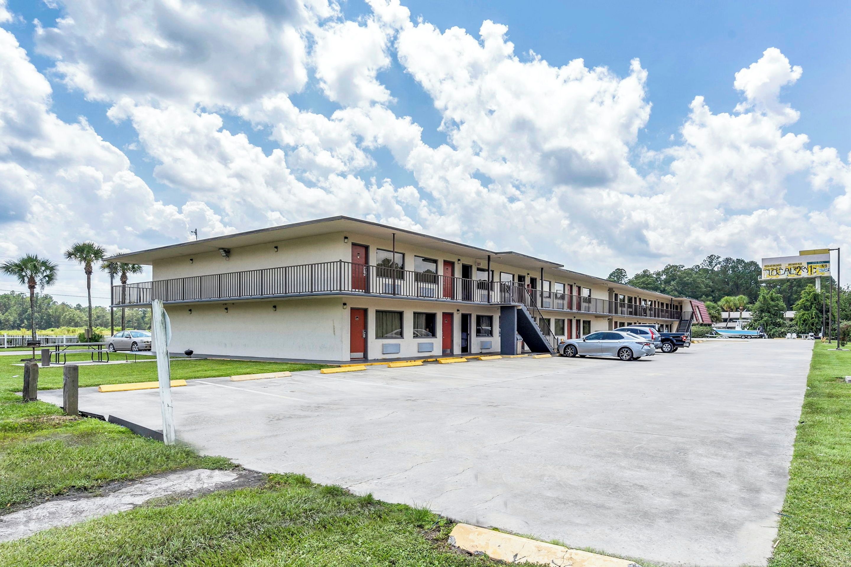 A motel with a two-story structure, a parking lot, and a clear sky with clouds. - Red Roof Inn MacClenny (MacClenny)