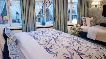 Habitación de hotel con una cama grande, una mesita de noche, una lámpara y vistas a edificios.