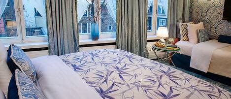 A hotel room with a large bed, a bedside table, a lamp, and a view of buildings outside.