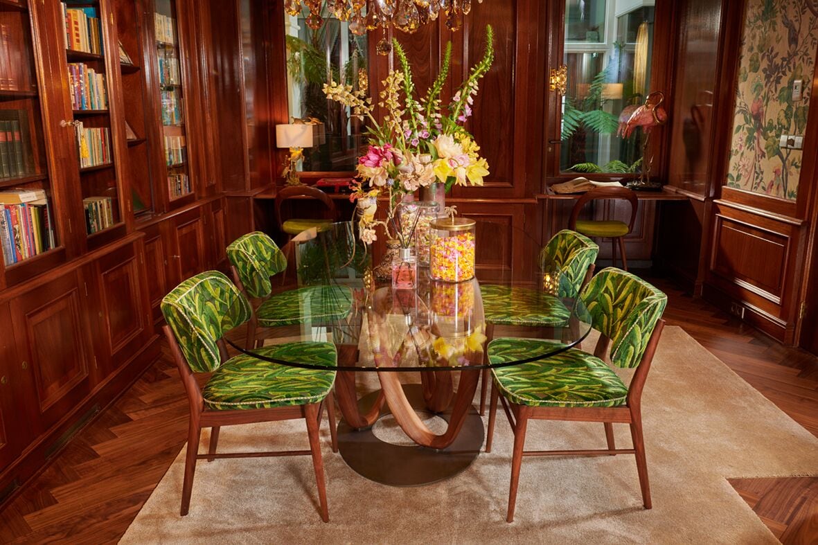 A dining room with a glass table surrounded by four chairs with green patterned upholstery.