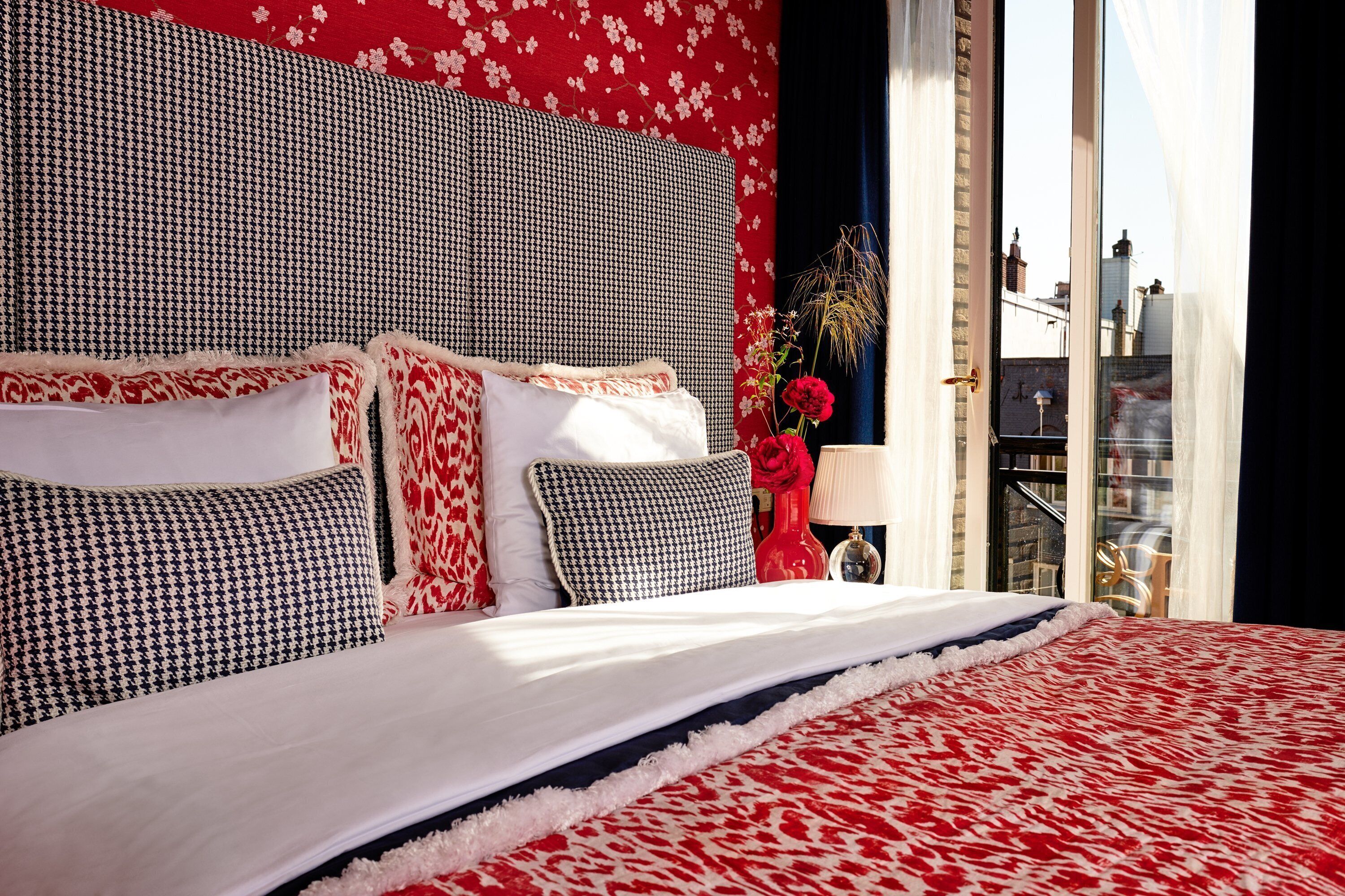 Ein Bett mit einer rot-weißen Bettdecke, einem houndstooth-Kopfstück und mehreren Kissen in Rot, Weiß und Schwarz-Weiß.