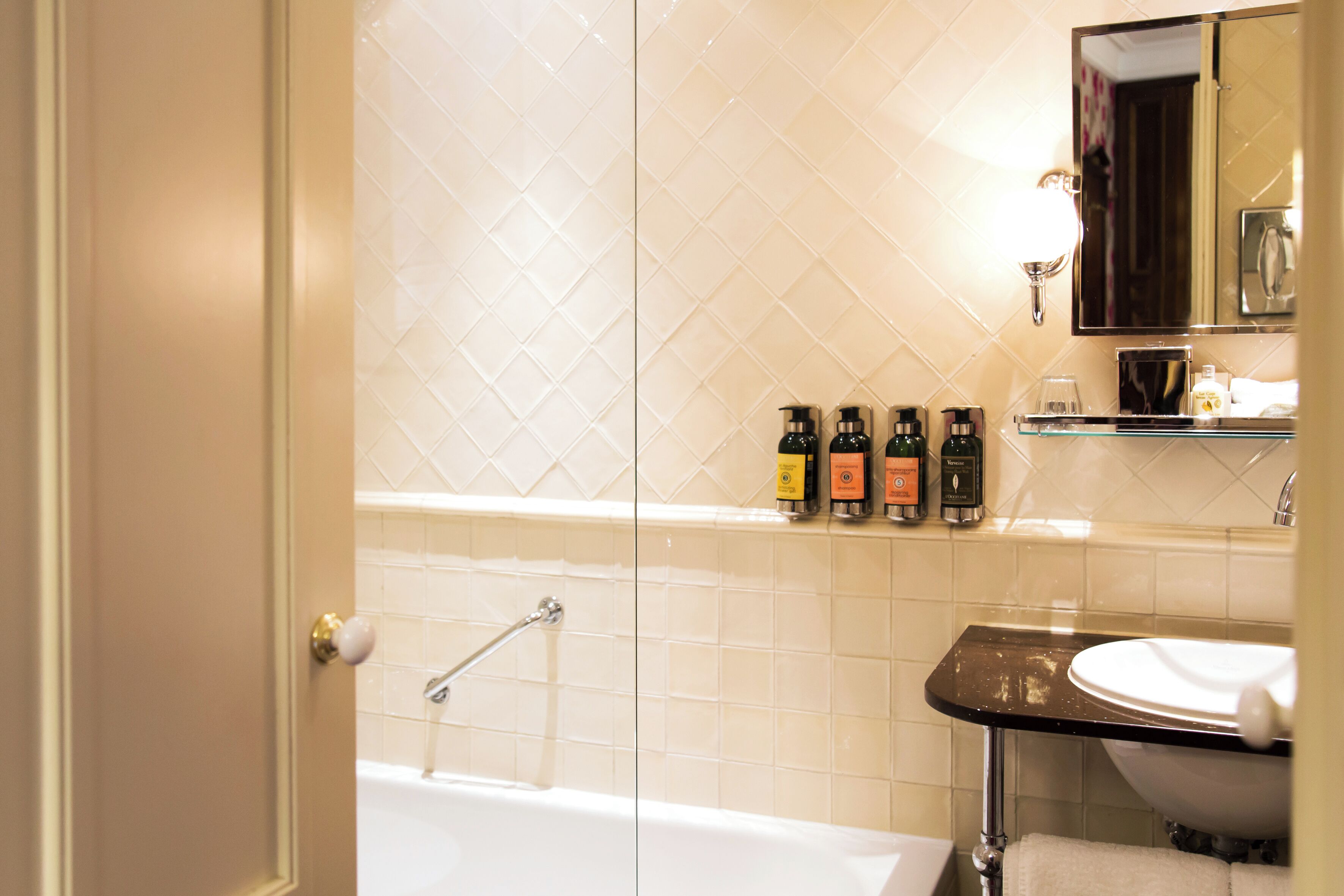 A bathroom with a bathtub, a sink, and a mirror. There are toiletries on the sink counter.