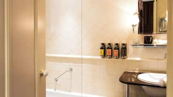 A bathroom with a bathtub, a sink, and a mirror. There are toiletries on the sink counter.