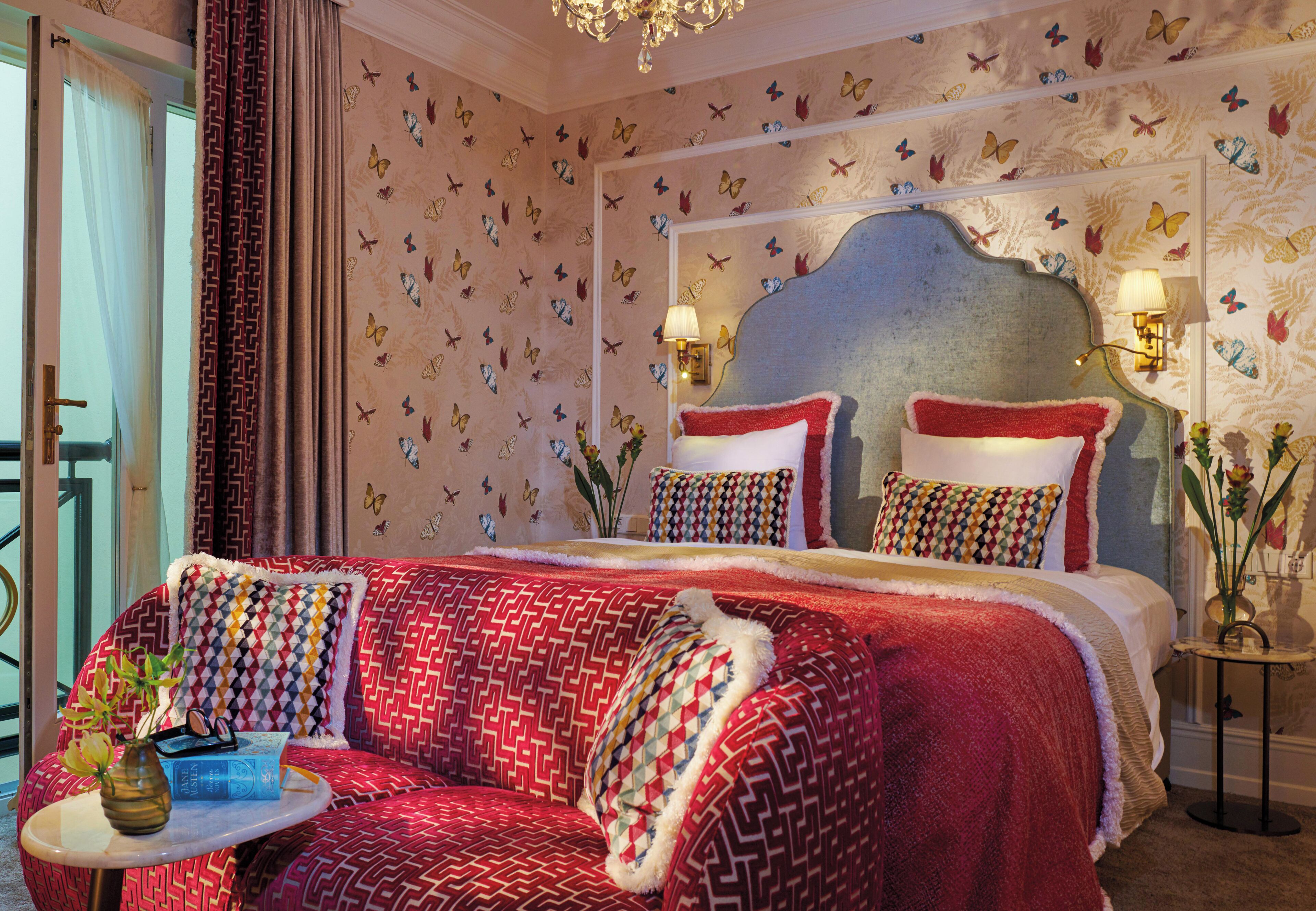 A bedroom with a patterned bedspread, a sofa with a patterned cushion, and a small table with a vase.