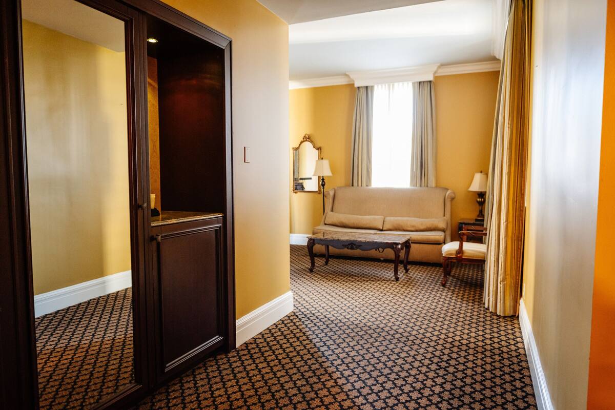 A hotel room with a patterned carpet, a sofa, a small table, and a mirror.