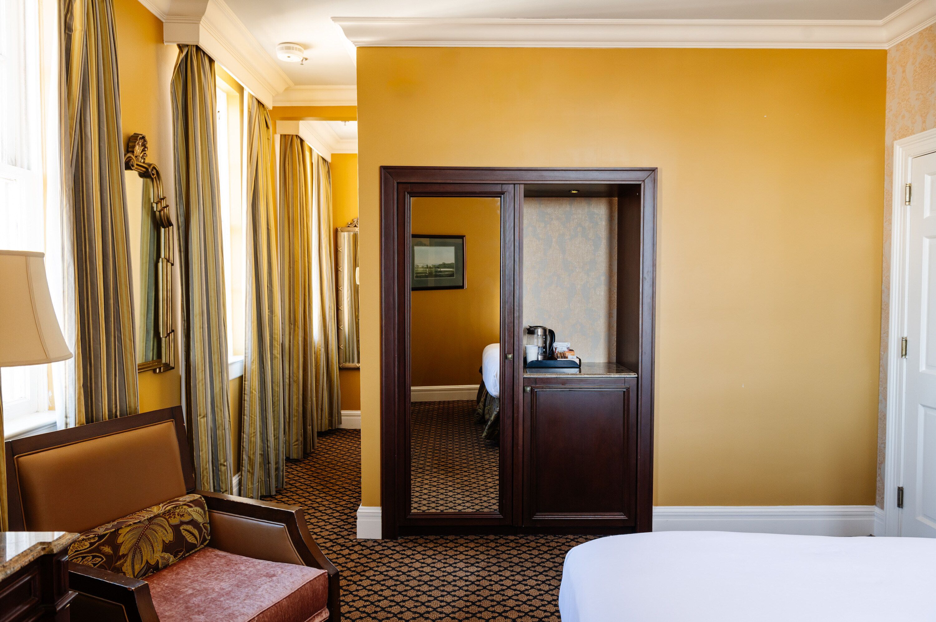 A hotel room with a bed, a desk, a chair, a bathroom visible through an open door, and a large mirror.