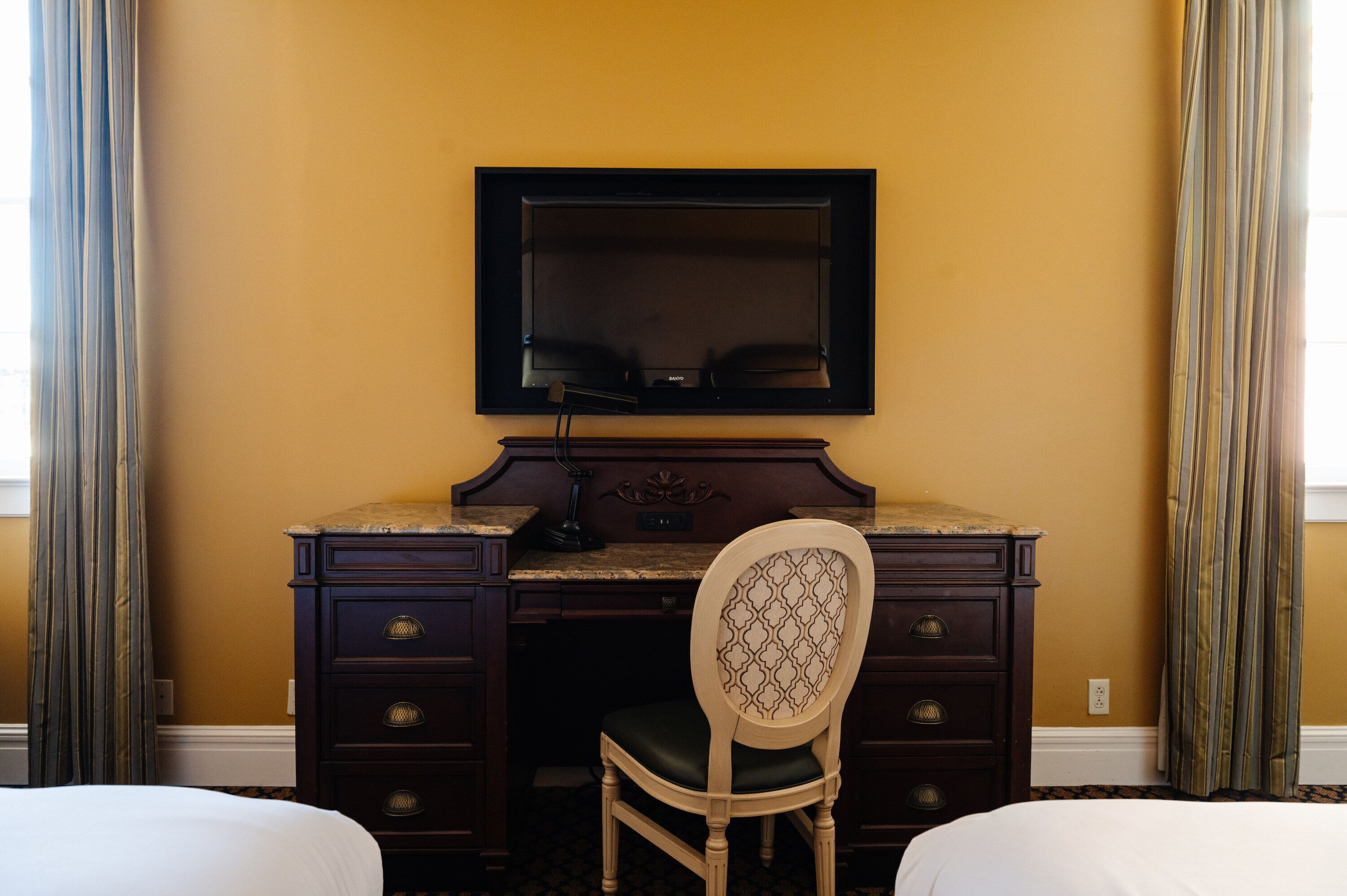 A hotel room with a dark wood desk, a chair, a flat-screen TV, and two beds.