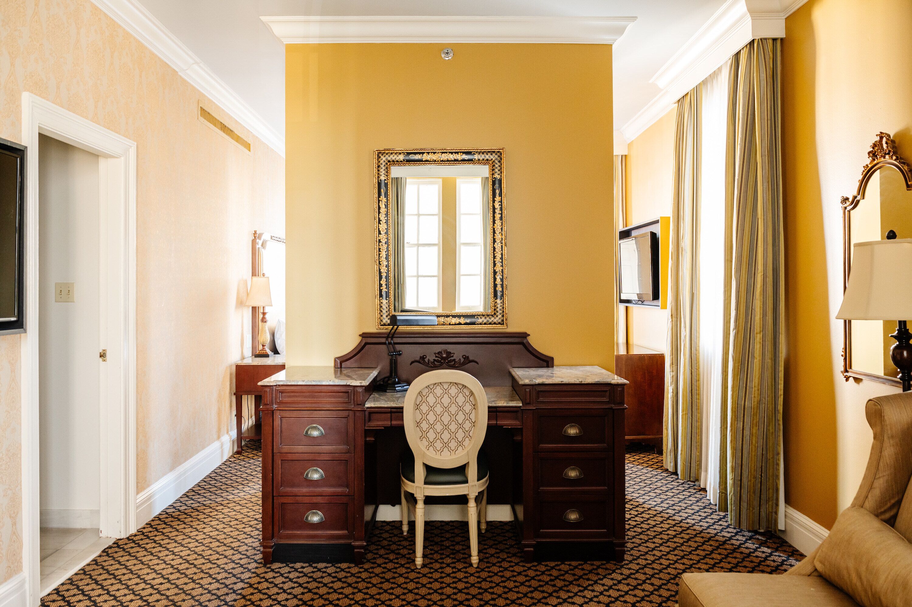 A hotel room with a desk, chair, and a large mirror.