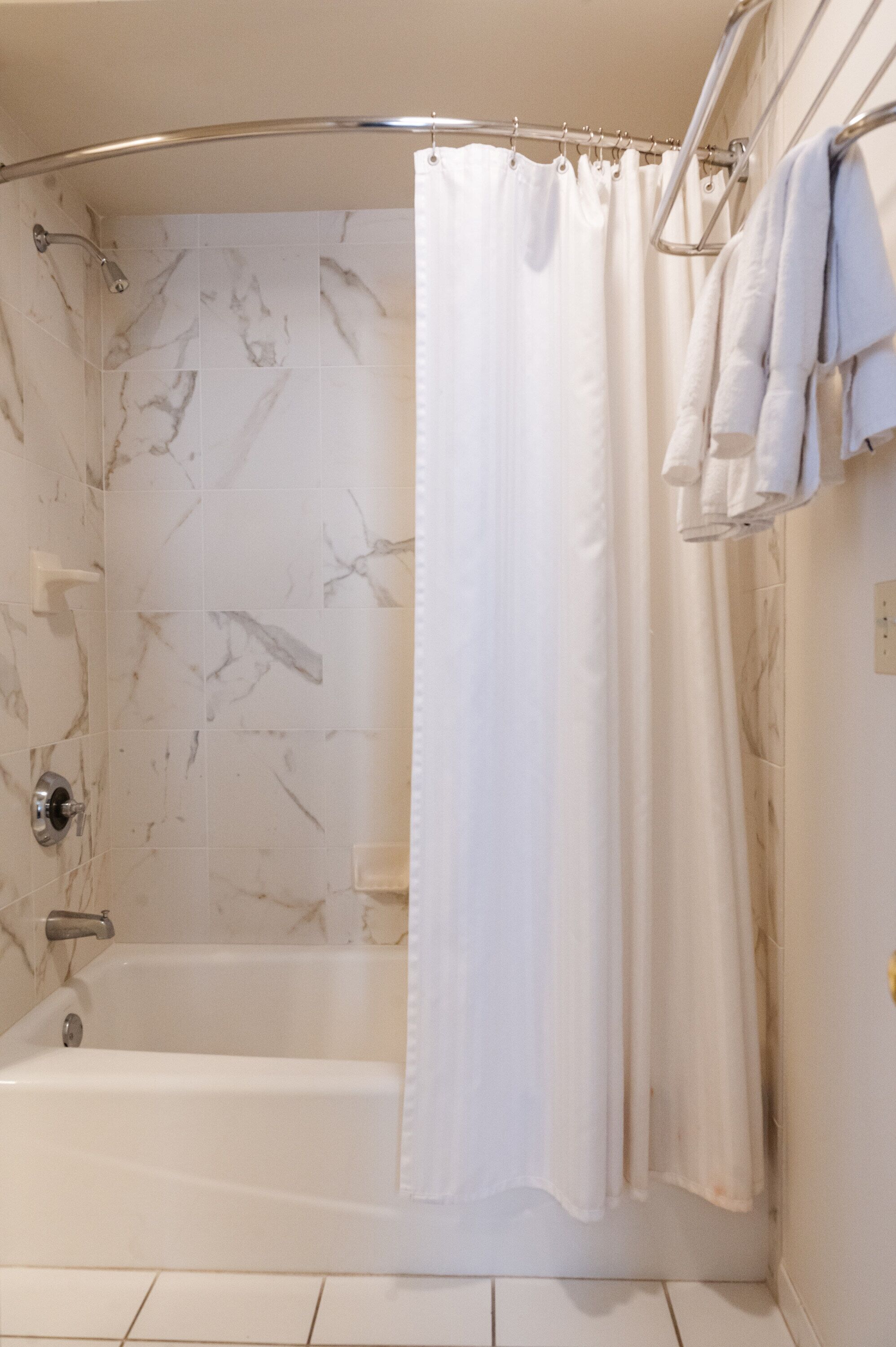 A bathroom with a shower, a bathtub, and a towel rack with towels.