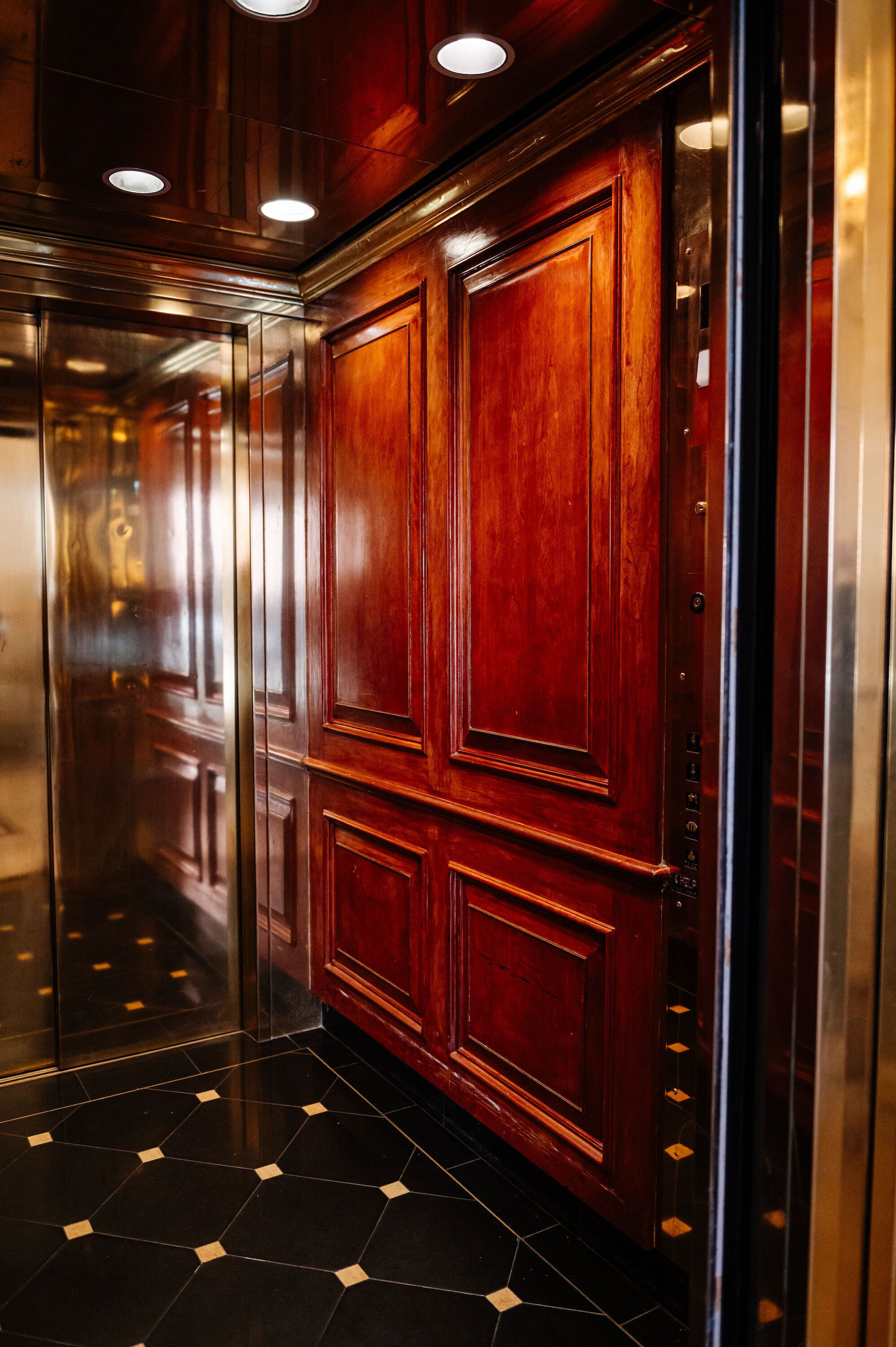 An elevator with wooden paneling and a reflective floor.