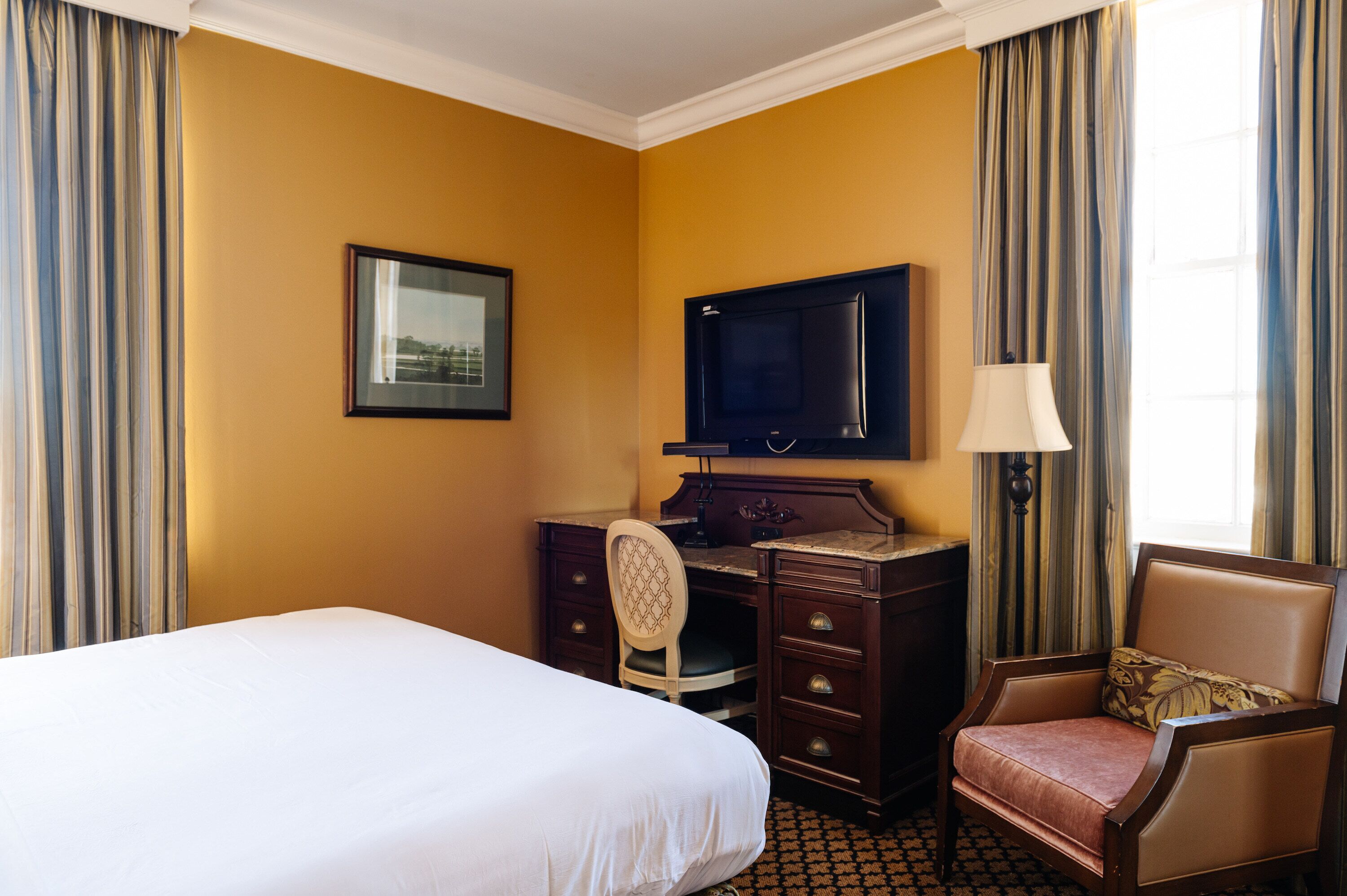 A hotel room with a bed, a desk, a chair, a television, and a lamp.
