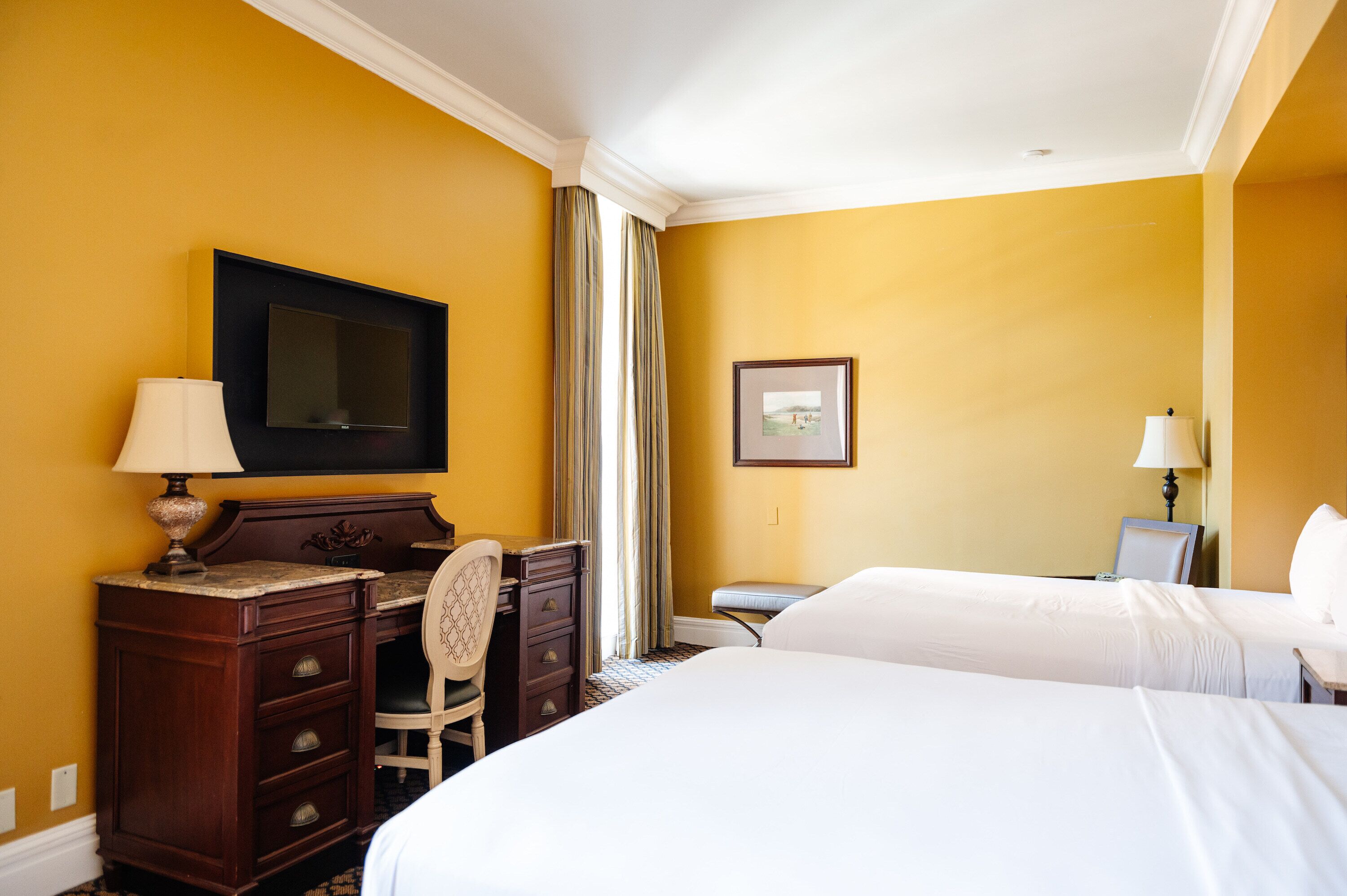 A hotel room with two beds, a desk with a chair, a TV, and a framed picture on the wall.