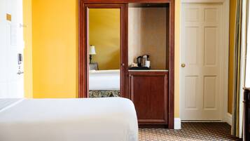A hotel room with a bed, a wooden door, a small table with a kettle, and a patterned carpet.