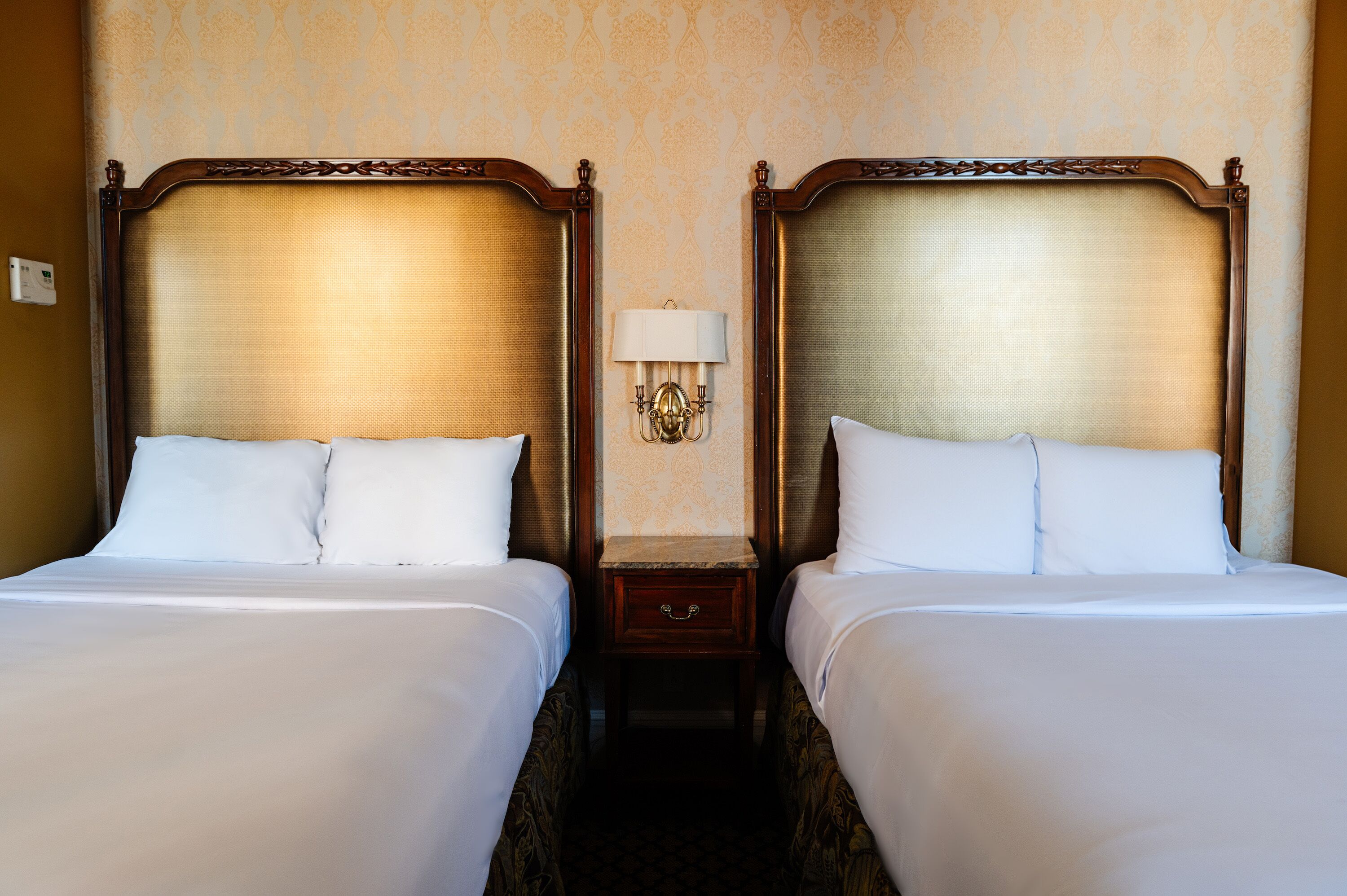 Ein Hotelzimmer mit zwei Betten, einem Nachttisch mit Lampe und einer Wandleuchte.