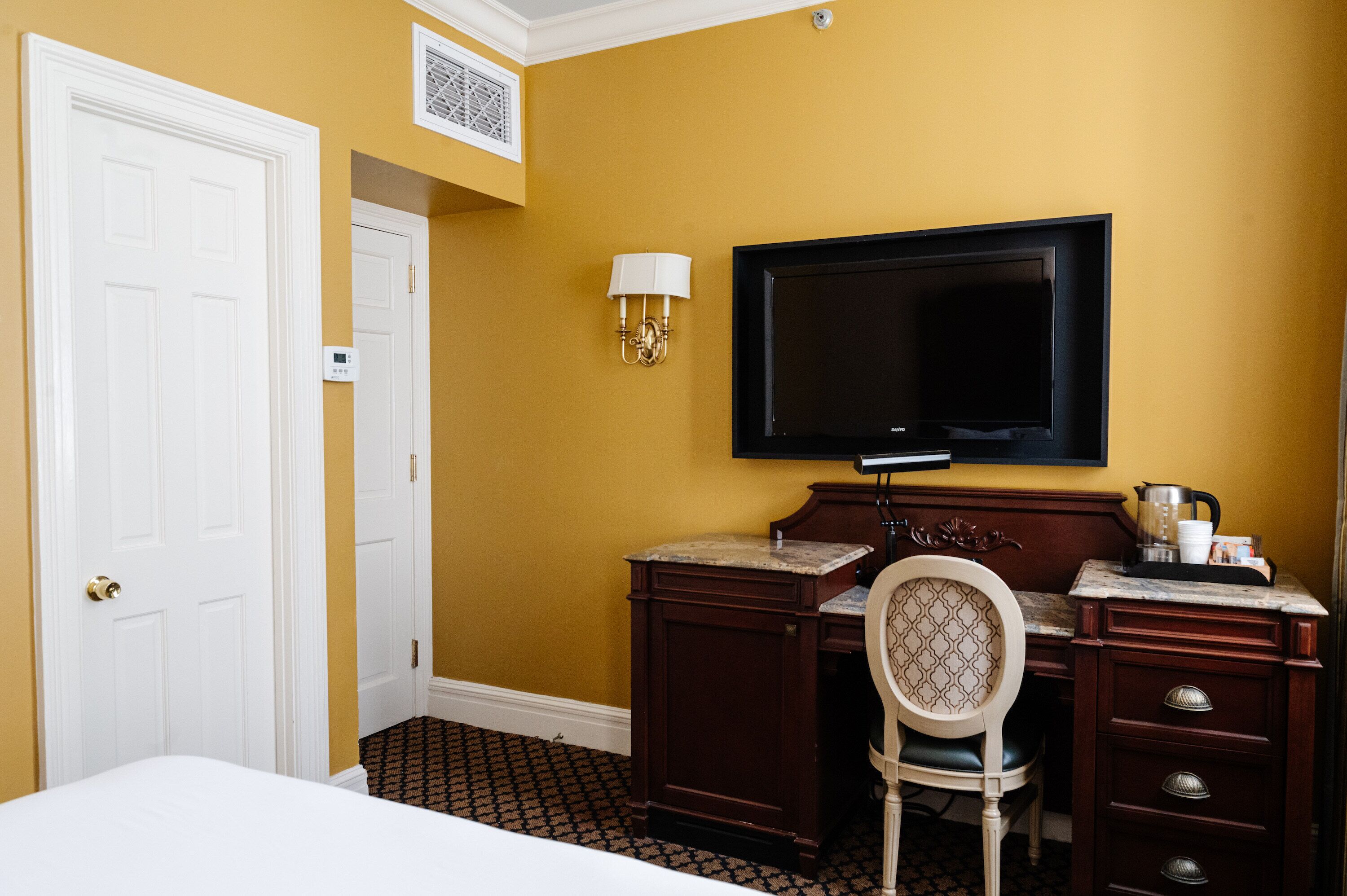Une chambre d’hôtel comprenant un lit, un bureau avec une chaise, une télévision et une lampe fixée au mur.