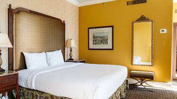 Una habitación de hotel con una cama grande, una mesita de noche, una lámpara, un cuadro enmarcado en la pared y un espejo.