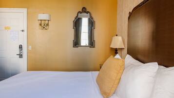 Una habitación de hotel con cama, una puerta, un espejo montado en la pared y una lámpara de pared.