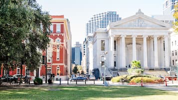 Una calle urbana con un edificio clásico que presenta columnas y una estatua, rodeado de modernos rascacielos.