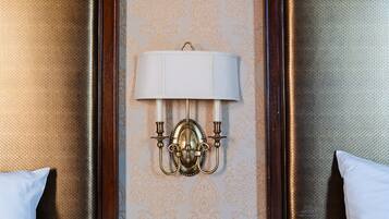 A hotel room with two beds, a nightstand with a lamp, and a wall-mounted light fixture.