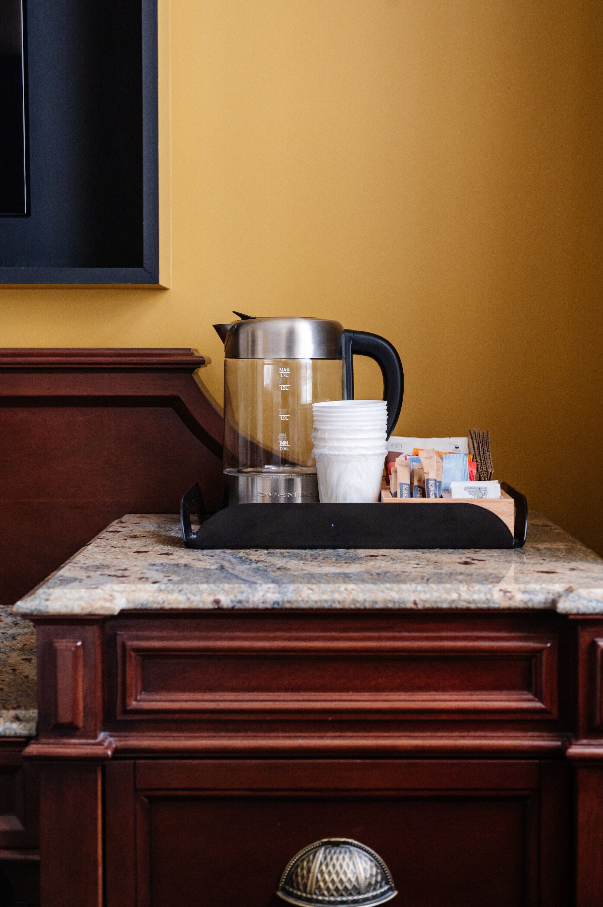 Una encimera de cocina con una cafetera, una pila de tazas blancas y un dispensador de cápsulas de café.