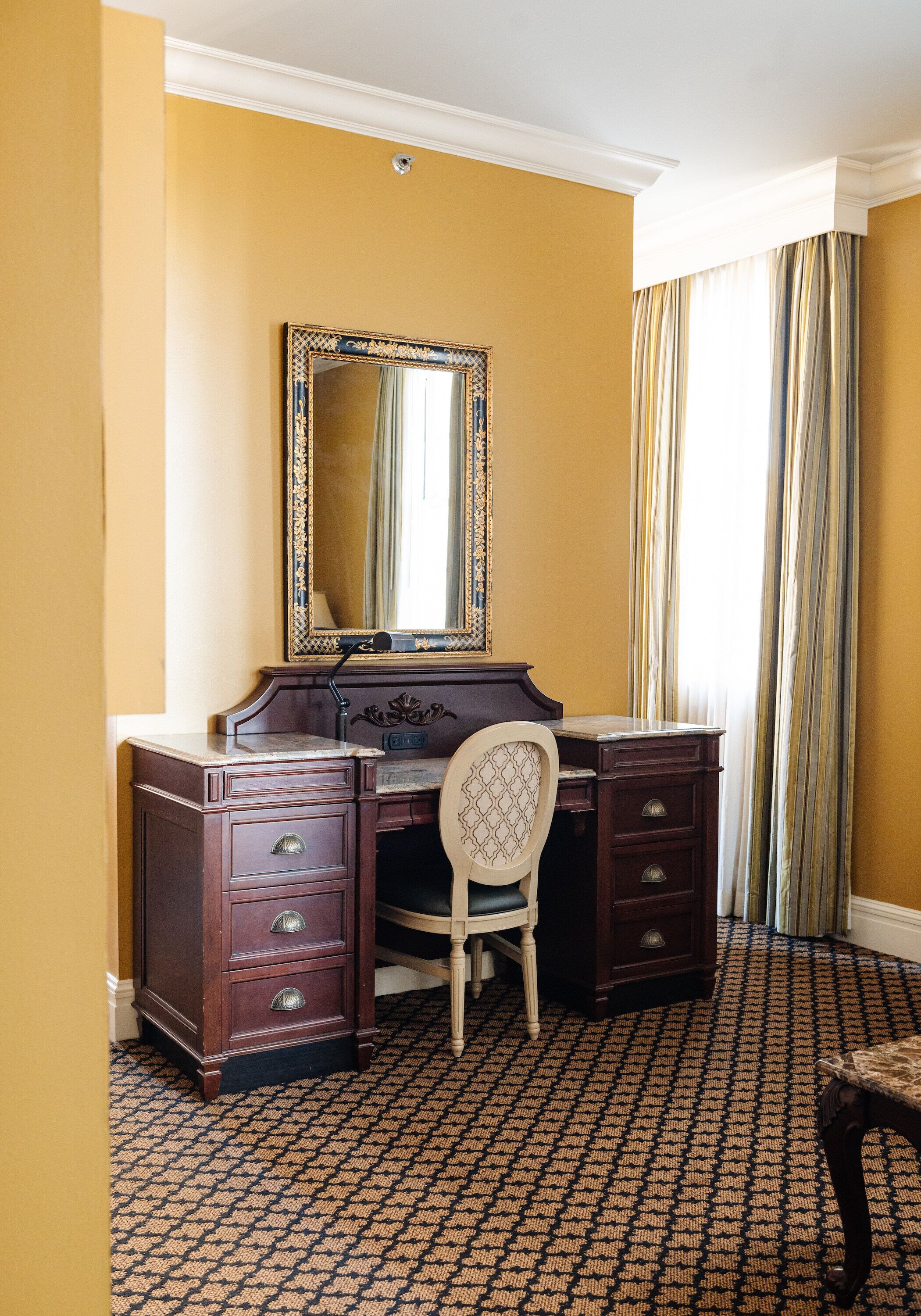 A room with a wooden desk, a chair, a large mirror, and a patterned carpet.