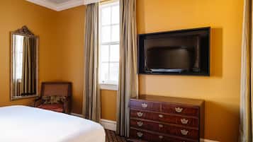 Habitación de hotel con una cama grande, un aparador, un televisor montado en la pared y una ventana con cortinas.