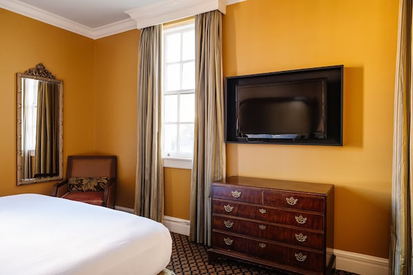 Habitación de hotel con una cama grande, un aparador, un televisor montado en la pared y una ventana con cortinas.