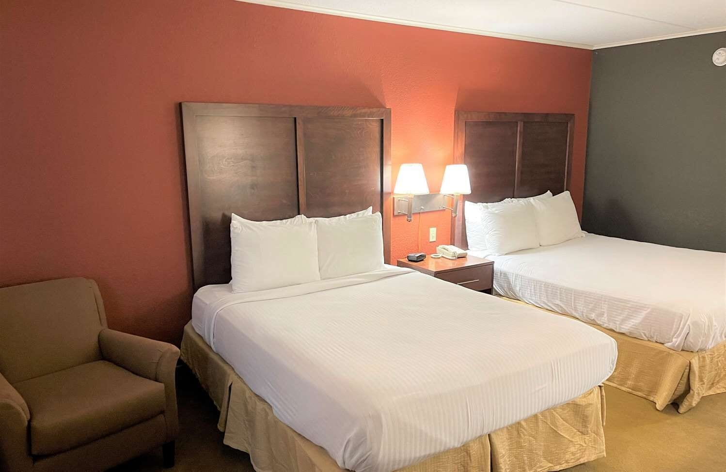 Habitación de hotel con dos camas, una silla y una mesita de noche con lámparas.