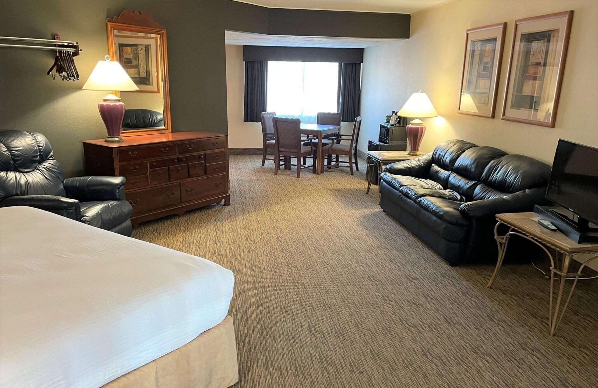 Habitación de hotel con cama, sofá de cuero, televisión, escritorio con dos sillas y cómoda.