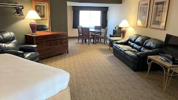 Habitación de hotel con cama, sofá de cuero, televisión, escritorio con dos sillas y cómoda.