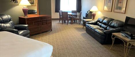 A hotel room with a bed, a leather sofa, a TV, a desk with two chairs, and a dresser.