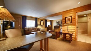 A cozy living room with a fireplace, a television, a sofa, and a dining table. - Crossroads Hotel and Event Center (Fort Dodge)