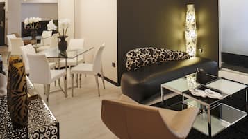 Una sala de estar moderna con una mesa de centro de vidrio, un sofá de cuero negro y un comedor con sillas blancas y una mesa de vidrio.