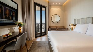Une chambre d’hôtel avec un grand lit, un bureau avec une chaise, un téléviseur fixé au mur, un miroir rond et un balcon avec des rideaux.