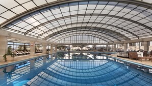 Une piscine intérieure dotée d’un toit en verre, de chaises longues et de plantes en pot.