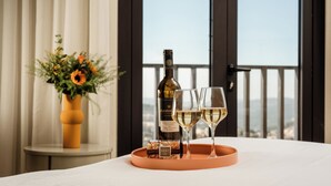Une table avec une bouteille de vin et deux verres sur un plateau, un vase rempli de fleurs et une vue sur la ville à travers de grandes fenêtres.
