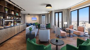 Un hall d’hôtel moderne doté d’un bar, d’un espace salon et de grandes fenêtres offrant une vue sur la ville.